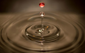A drop of water dropping into a still pool of water and creating a ripple effect 