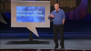 wayne dyer speaking at a conference with a projector screen reading 'when you correct your mind, everything falls into place'